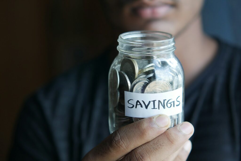 A hand holding a jar labeled savings with coins