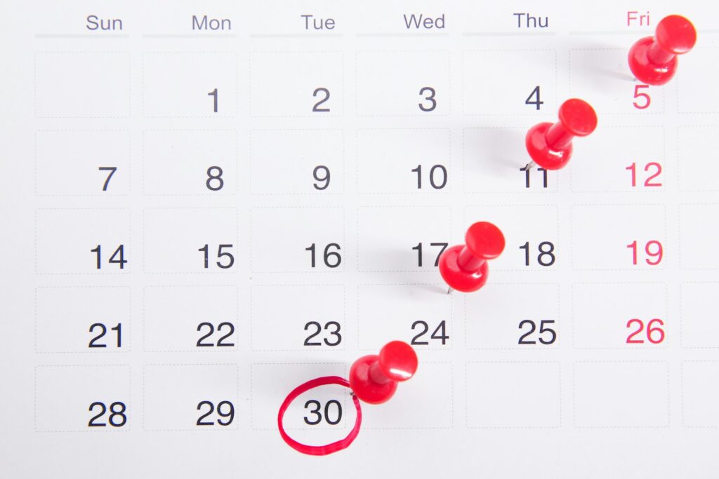 A calendar with red push pins marking key dates